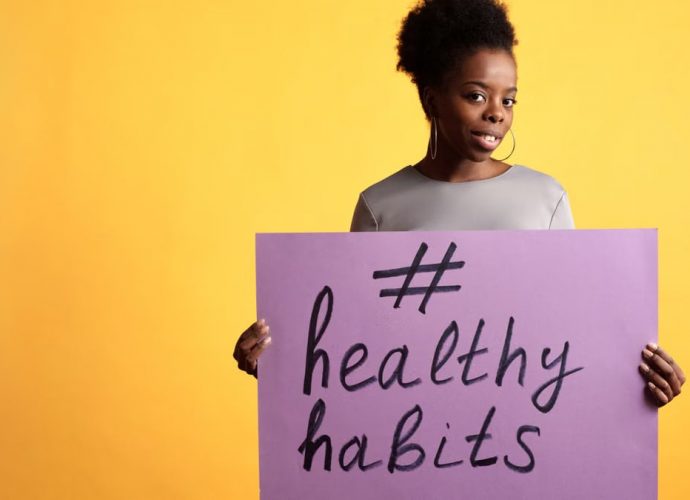 Portrait of a woman holding a healthy habits sign, set against a vibrant yellow background.