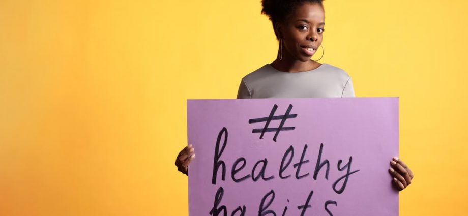 Portrait of a woman holding a healthy habits sign, set against a vibrant yellow background.